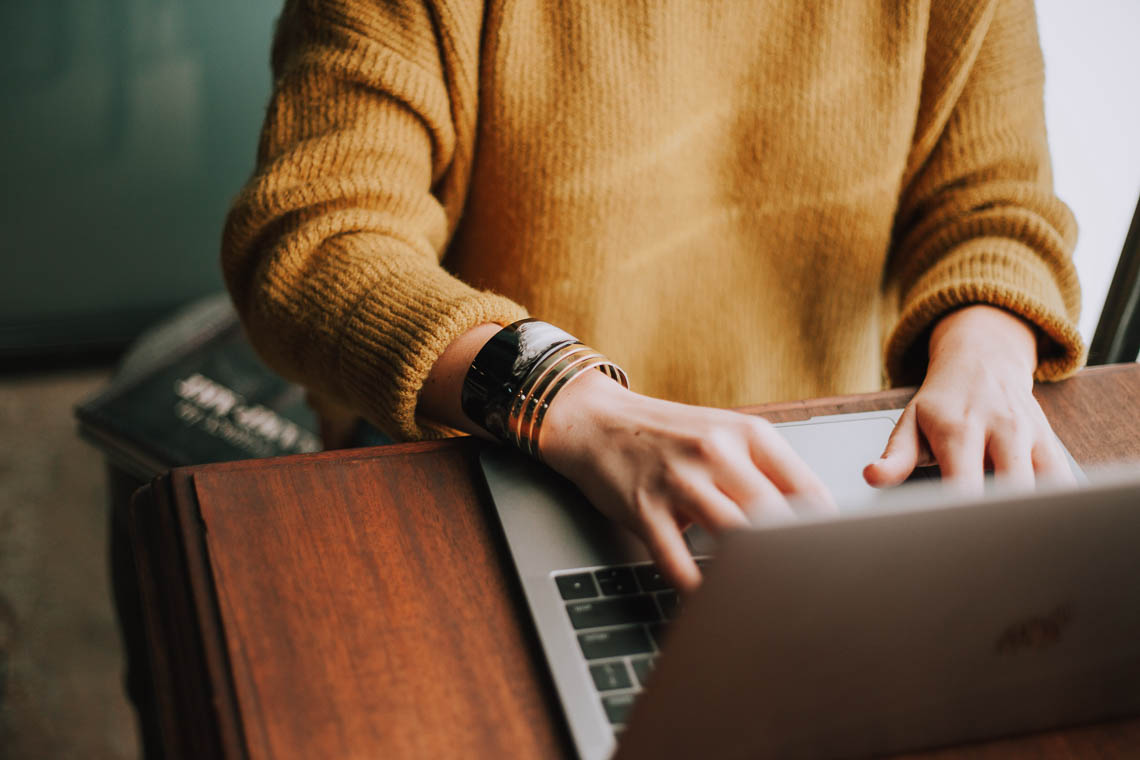 Close up of a person in a yellow sweater typing on a laptop keyboard