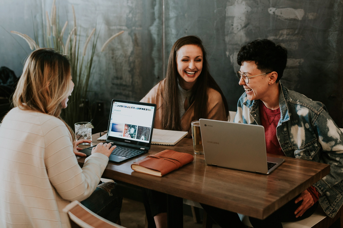 Three people sitting at a table with laptops and laughing