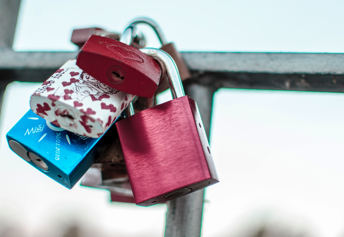 A cluster of pink and blue padlocks attached to an iron grate