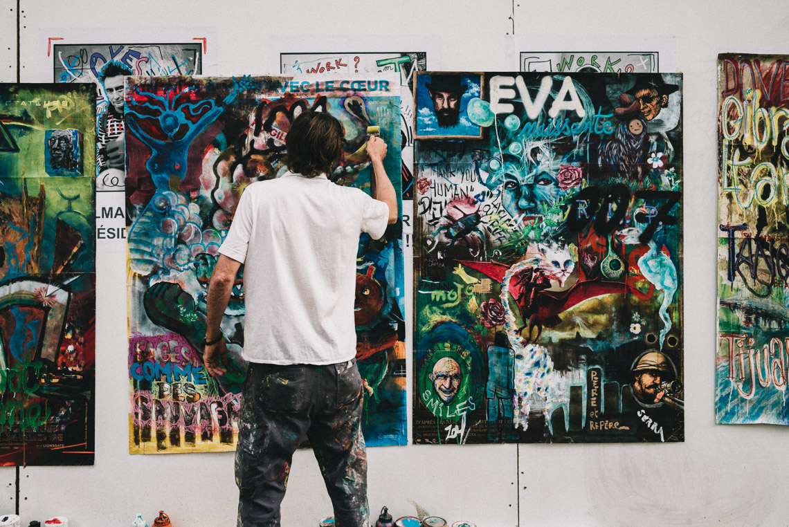 Man standing in front of a wall while painting on a graffiti-style poster