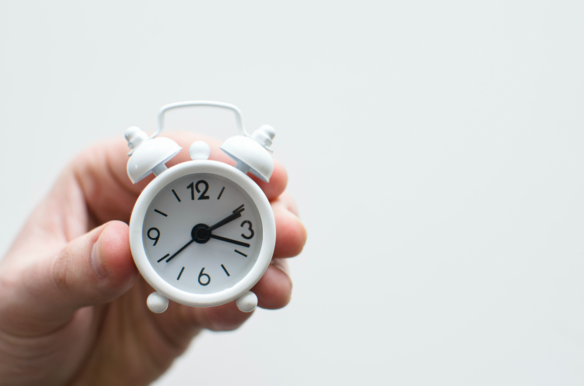 A hand holding a small clock on a white background