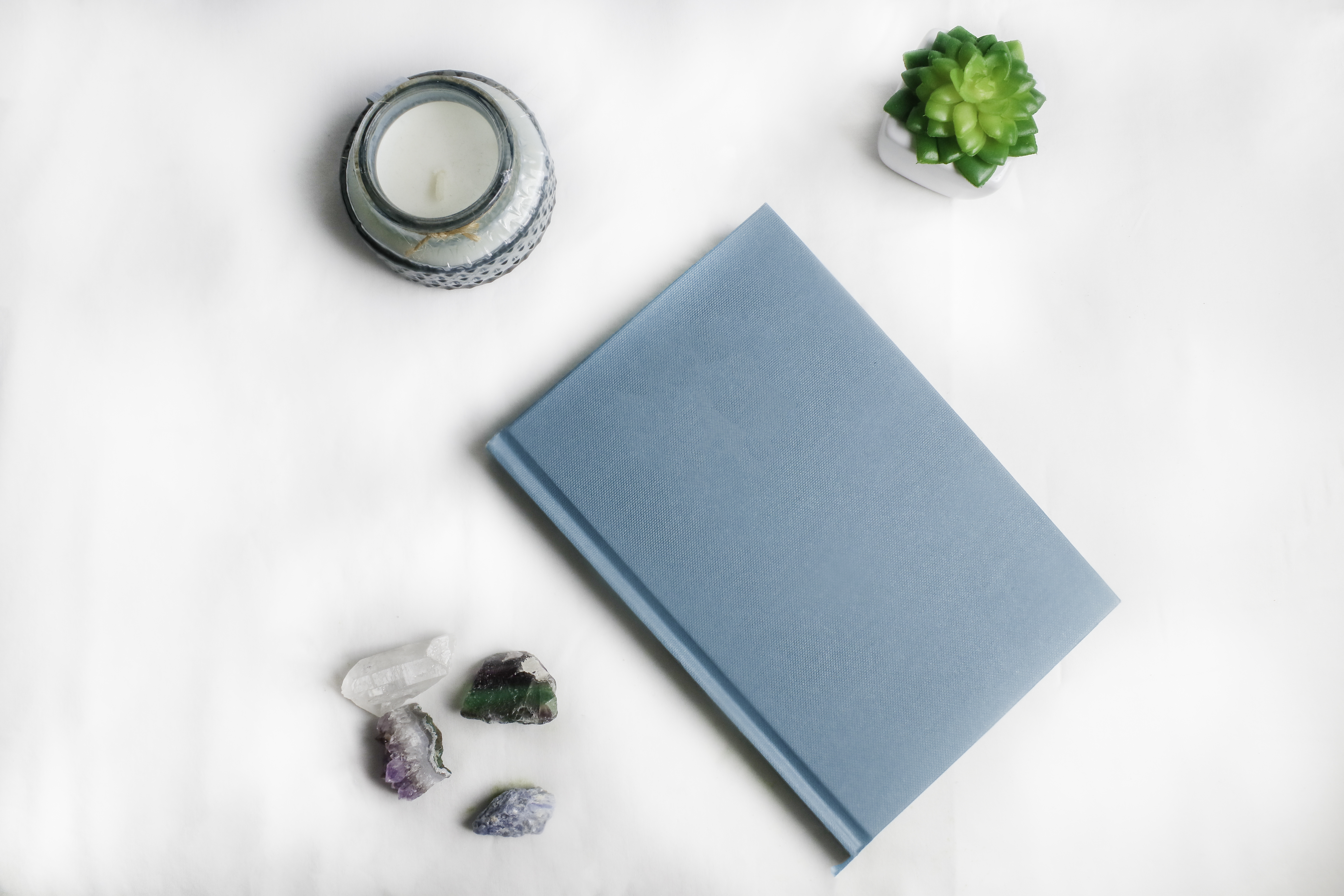 A blue notebook on a white background with some candles and crystals
