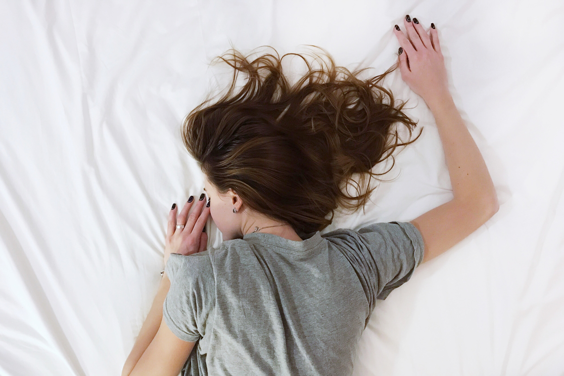 Girl laying face-down on a white bed.