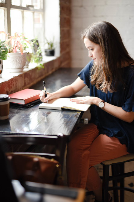 Woman sitting at a desk by a window writing in a notebook