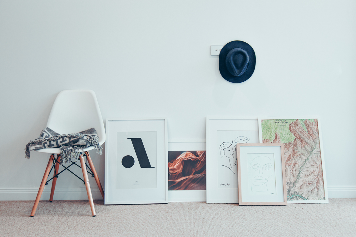 A chair and a bunch of photo frames sitting against a blank wall.