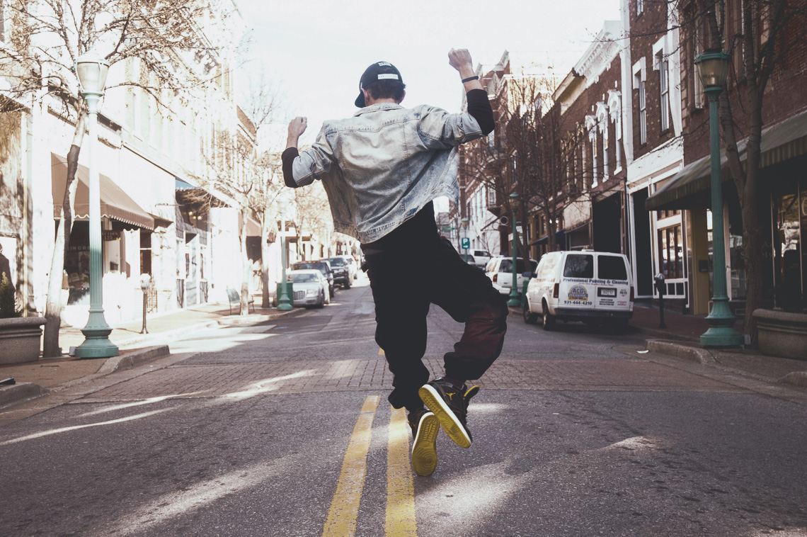 A man facing away from the camera and dancing down the middle of a street.