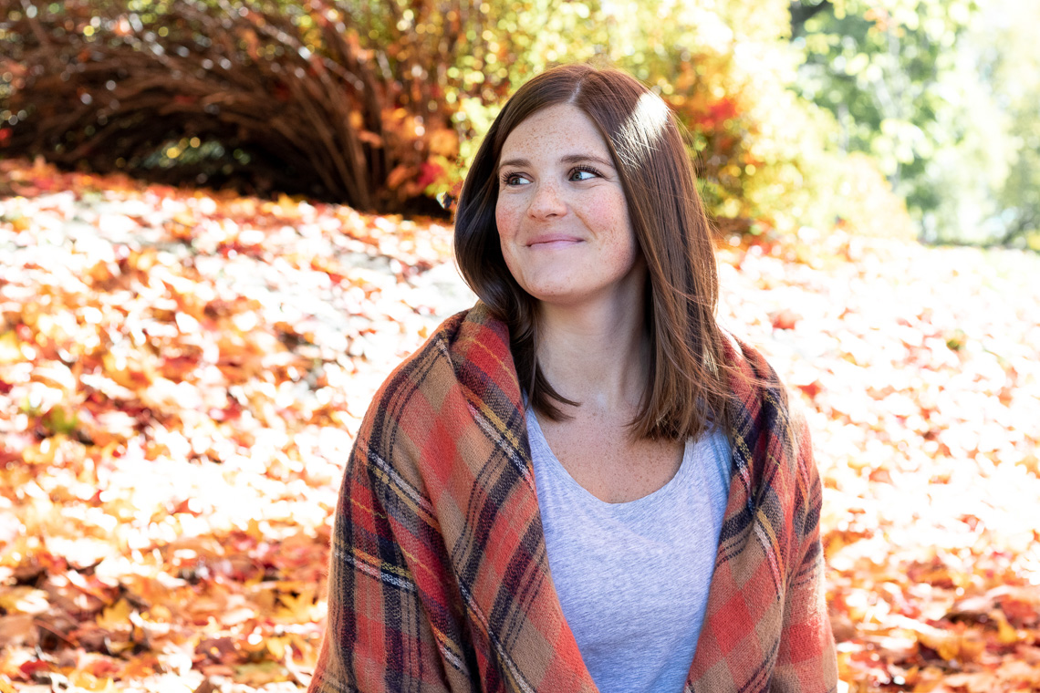 A woman looking away from the camera and smiling. She is wearing an orange plaid shawl.