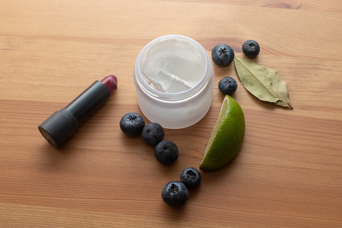 Cream, natural ingredients and a lipstick arranged on a wooden table.