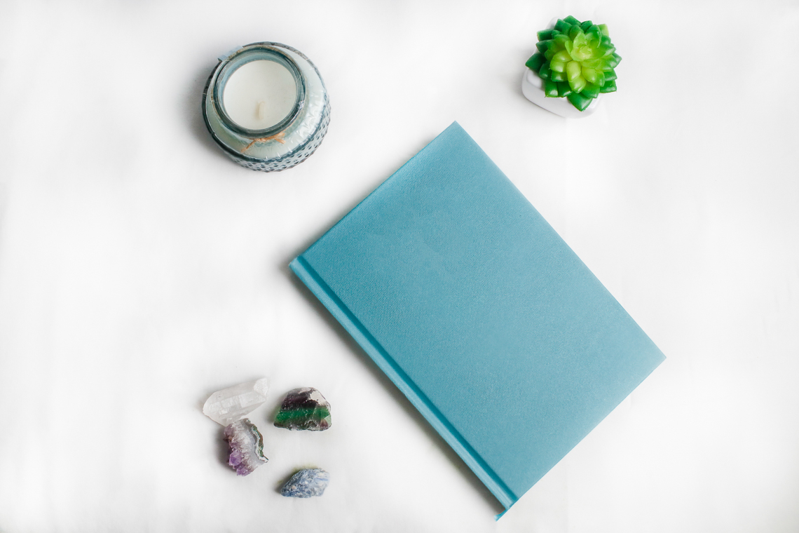 A blue notebook, a candle and some crystals on a white background.