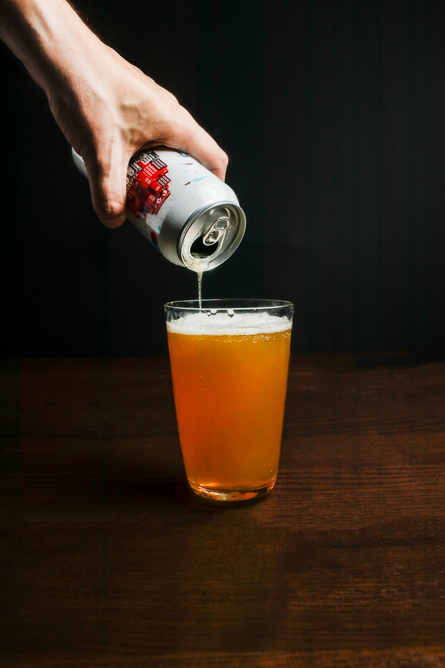 A man's hand pouring a can of beer into a clear glass.