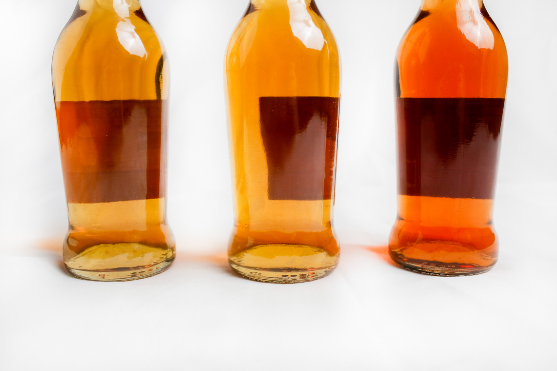 Three glass bottles with golden liquid on a white background. 