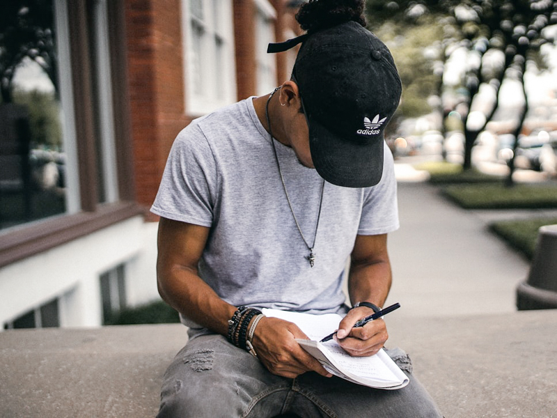 Black man writing in a notebook while sitting outside