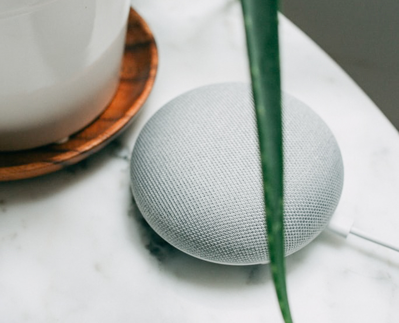 A grey Google Home device sitting on a marble table