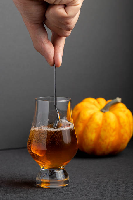 Man stirring a glass of golden beer with a spoon.