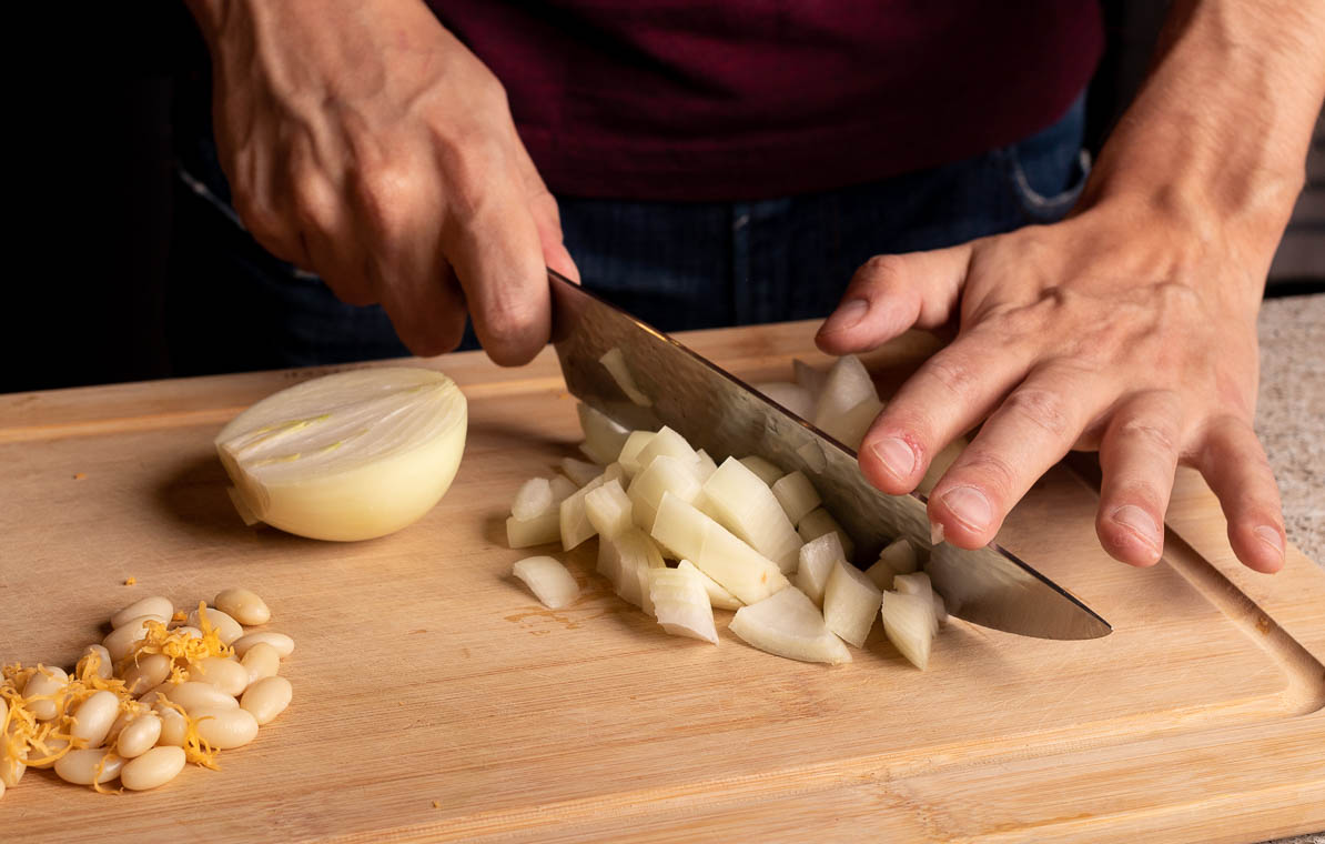 Man chopping onions with a chef's knife on a wood cutting board.