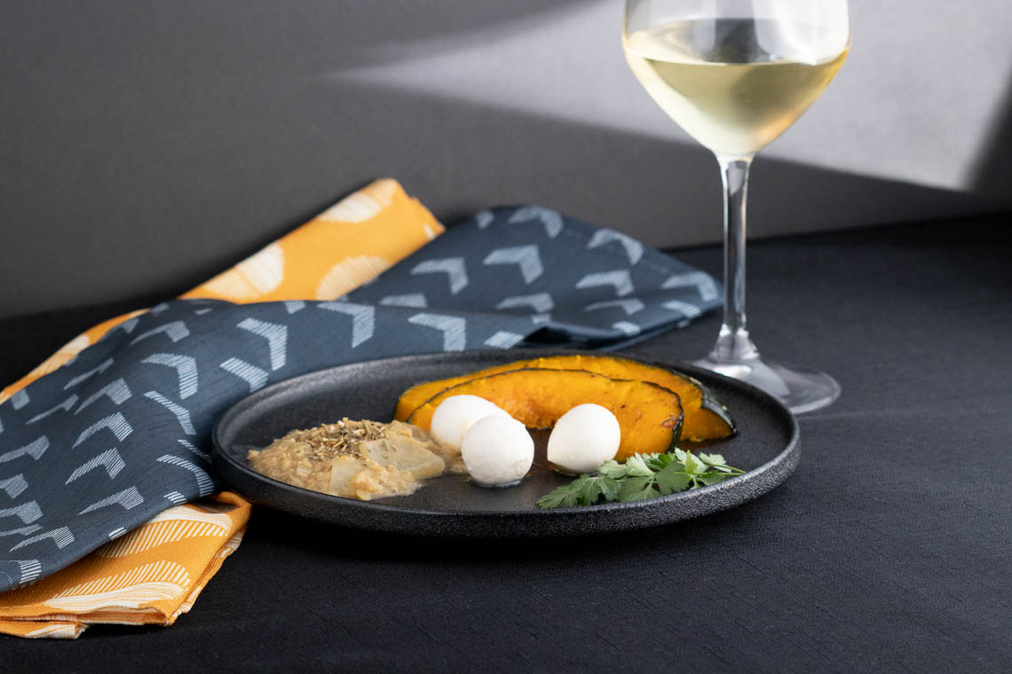 A meal of squash, mozarella and lentils on a black plate.