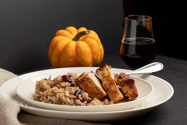 A warm winter meal of pork and rice on a white plate with beer and pumpkin in the background