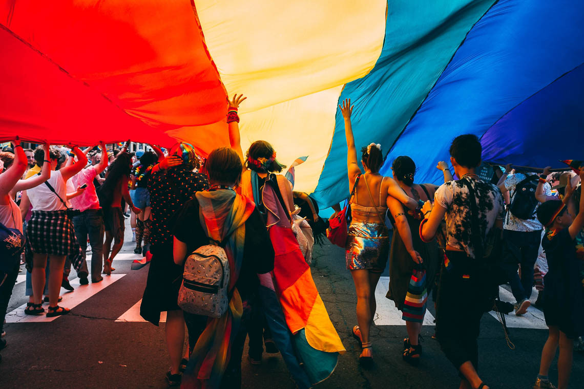 People marching in a Pride parade under a rainbow flag