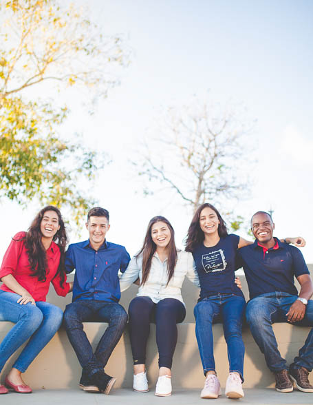 Five friends sitting on a bench with arms around each other