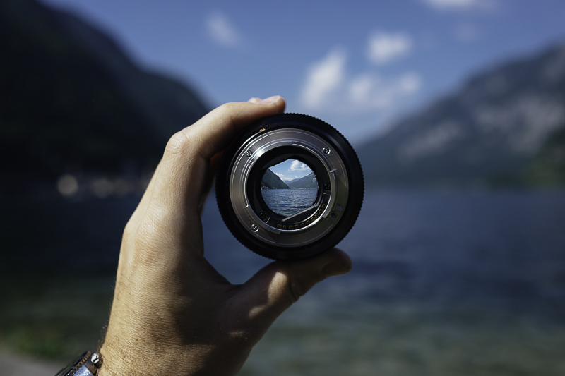 A hand a lens with mountains in focus in the lens glass.