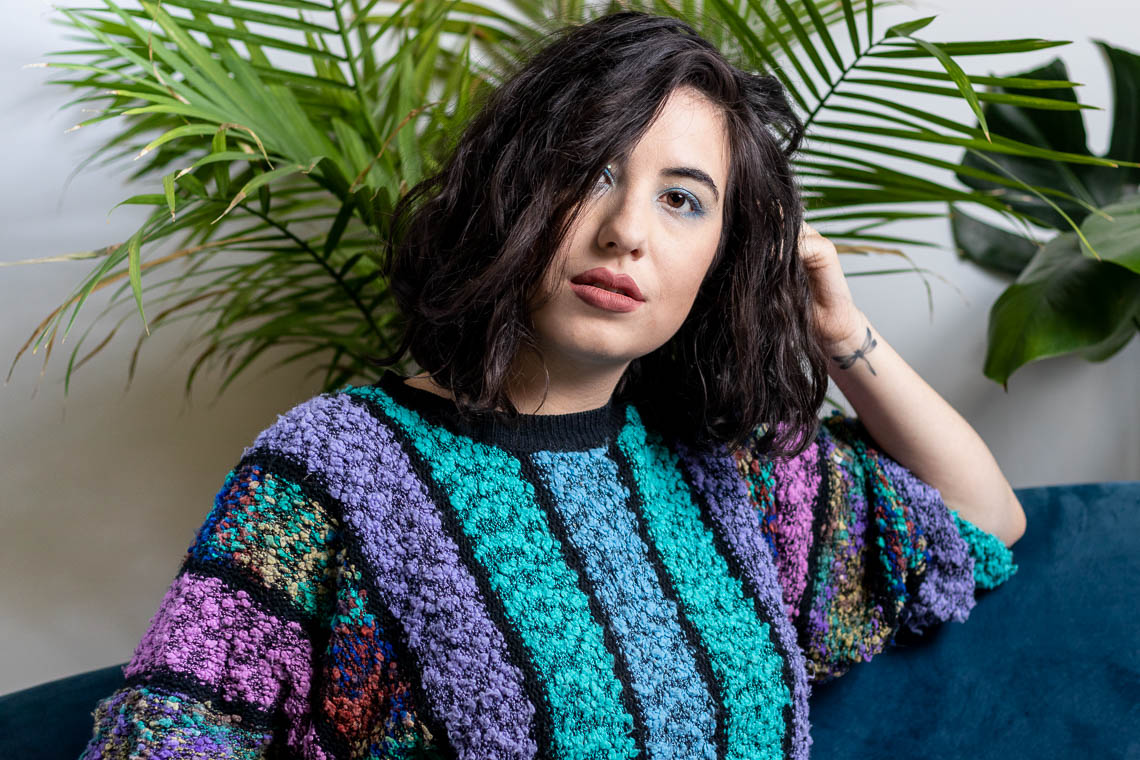 Headshot of a black-haired woman in a colourful sweater looking at the camera.