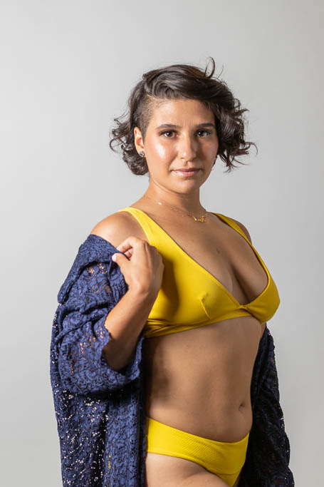 Portrait of a woman with short black hair wearing a yellow swimsuit and a blue lace coverup.