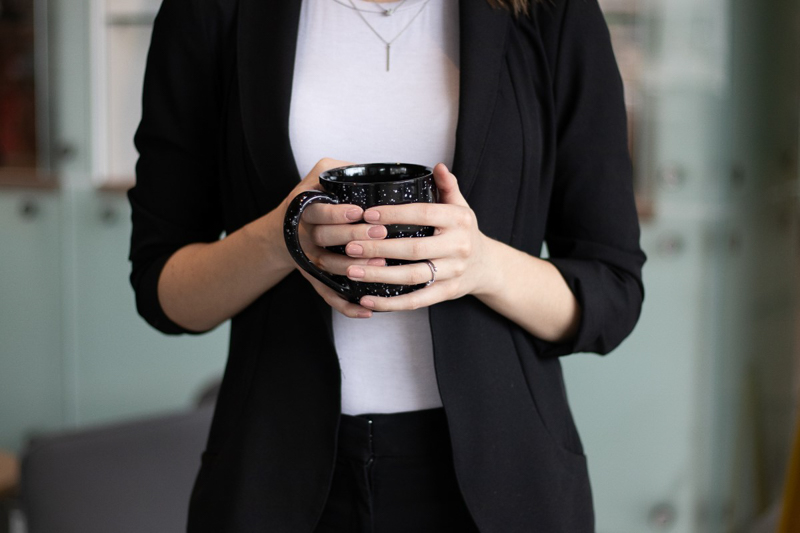 Woman wearing a business casual outfit holding a coffee mug.