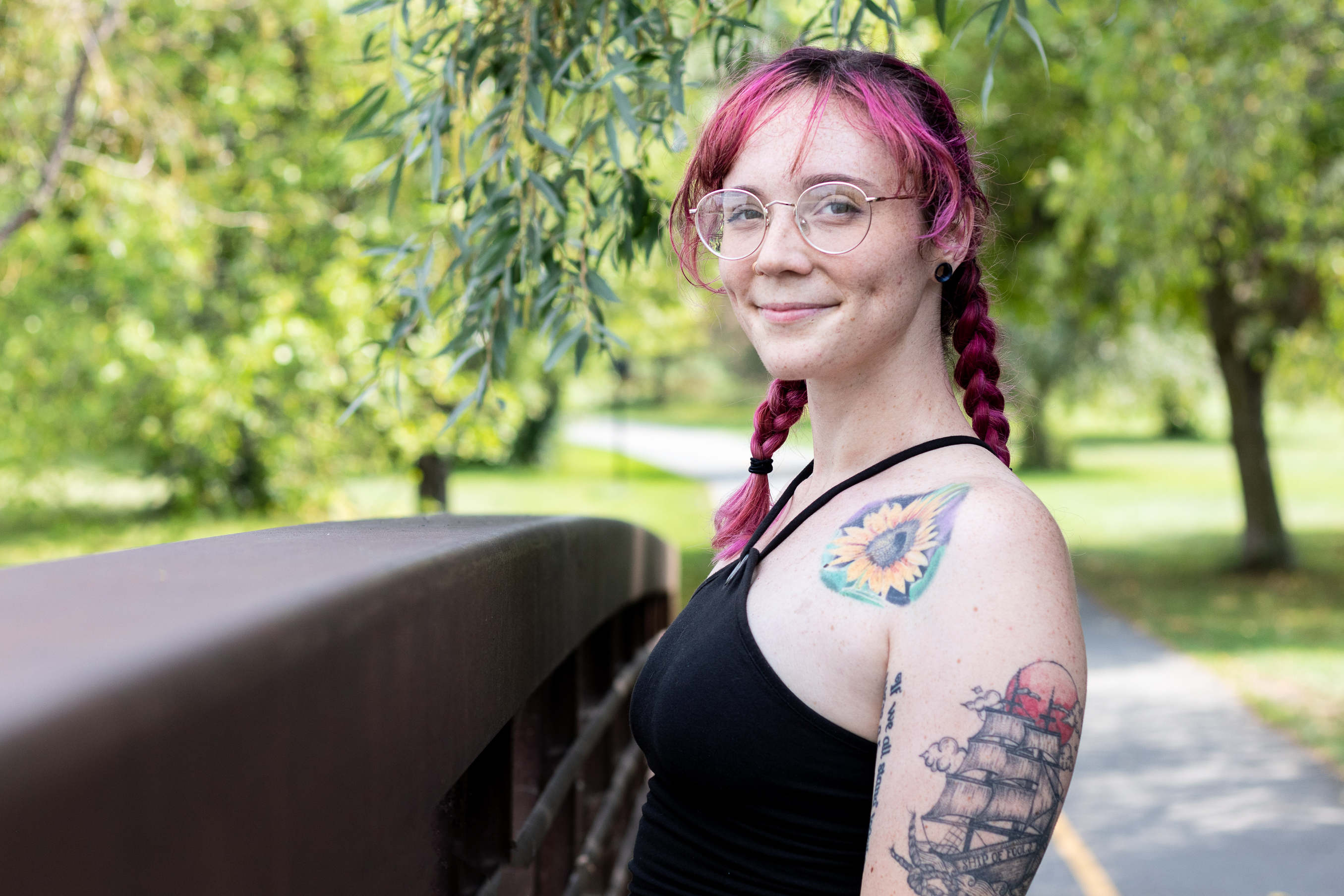 Head shot of a woman with pink braided hair standing outdoors.