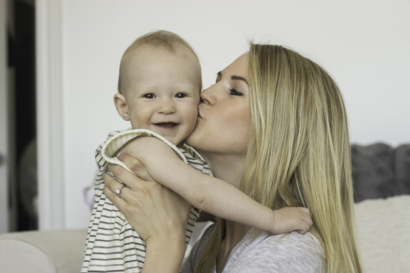 A blonde woman kissing a smiling baby on the cheek.