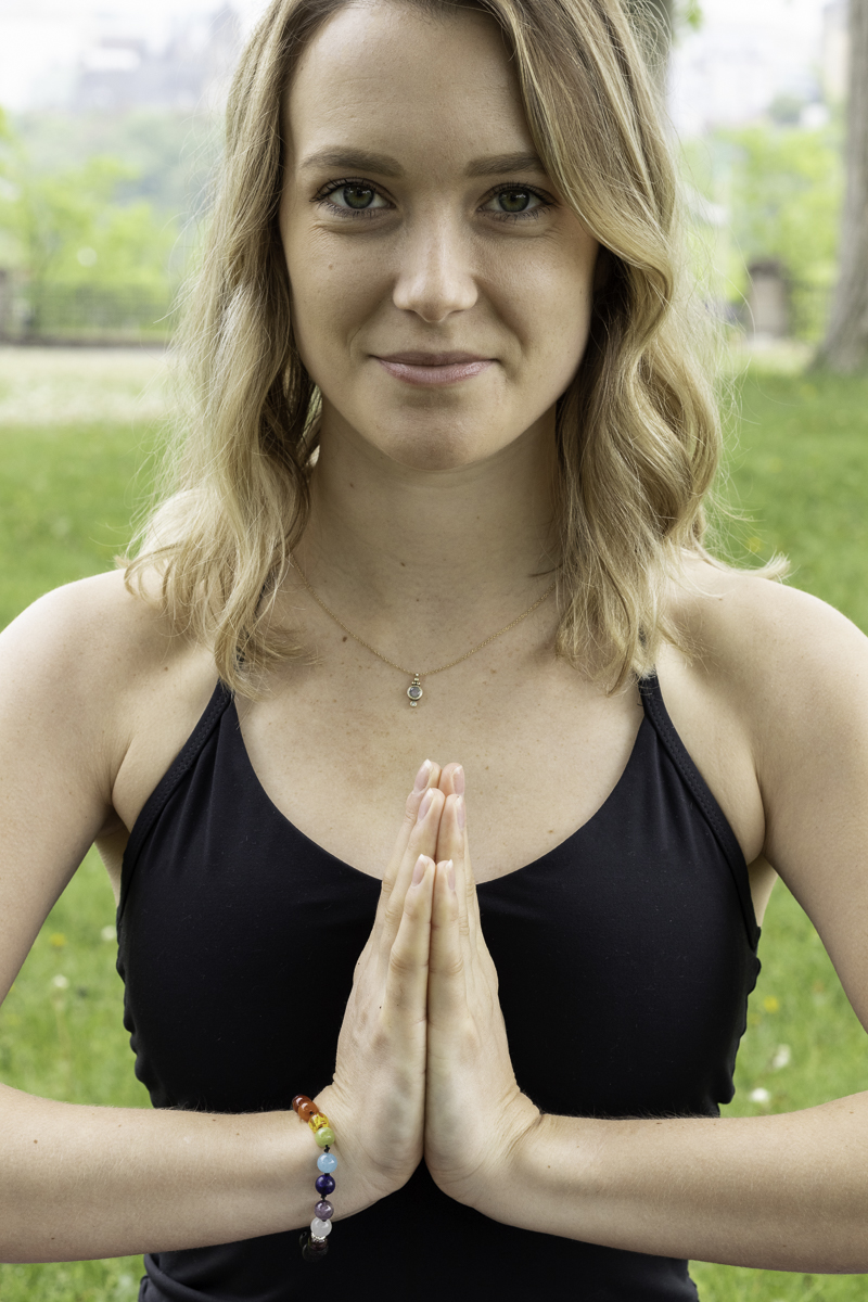 A close up of a blonde woman with hands in prayer position and looking at the camera.