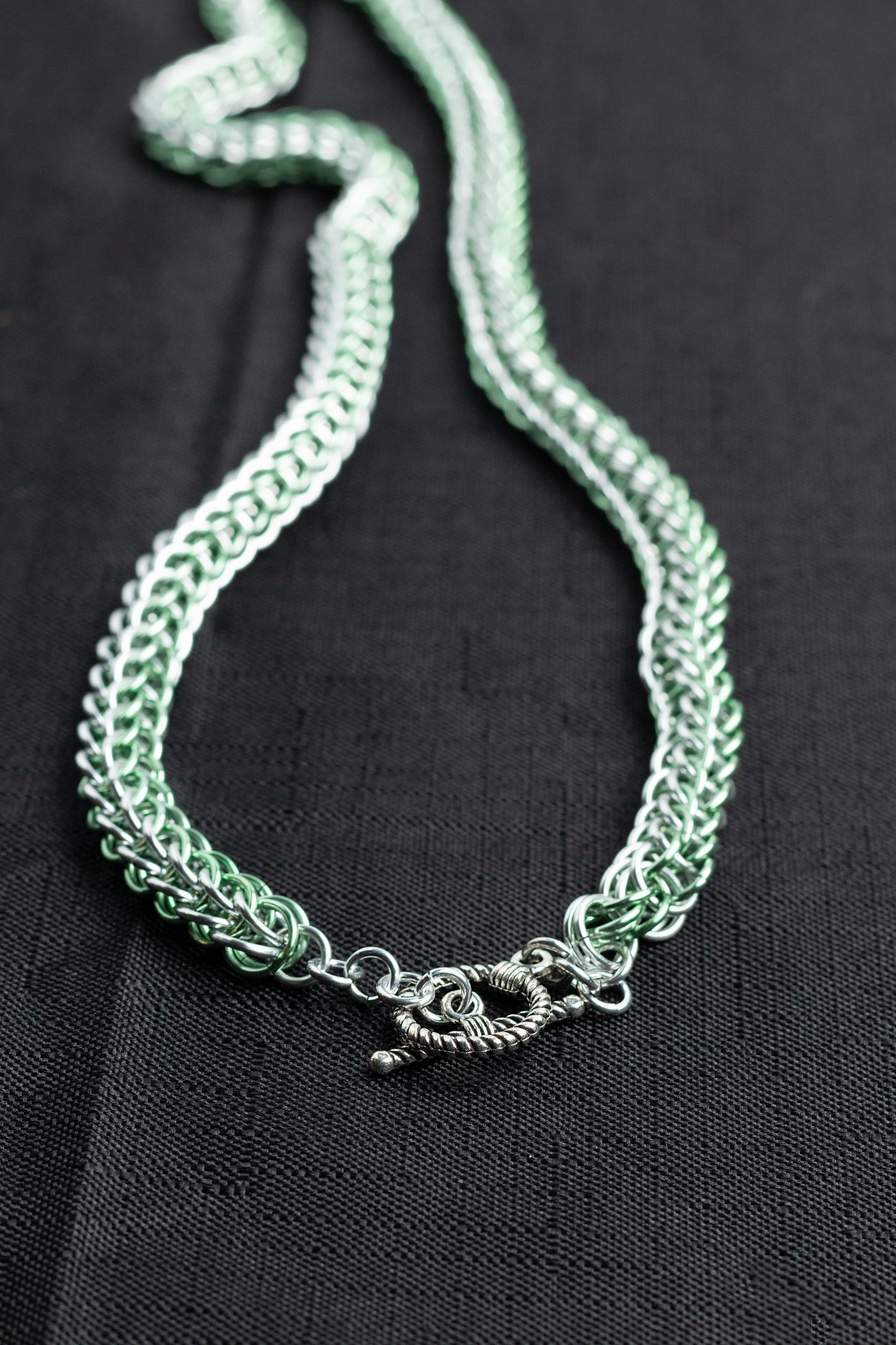 Silver and green chain necklace on a black background.
