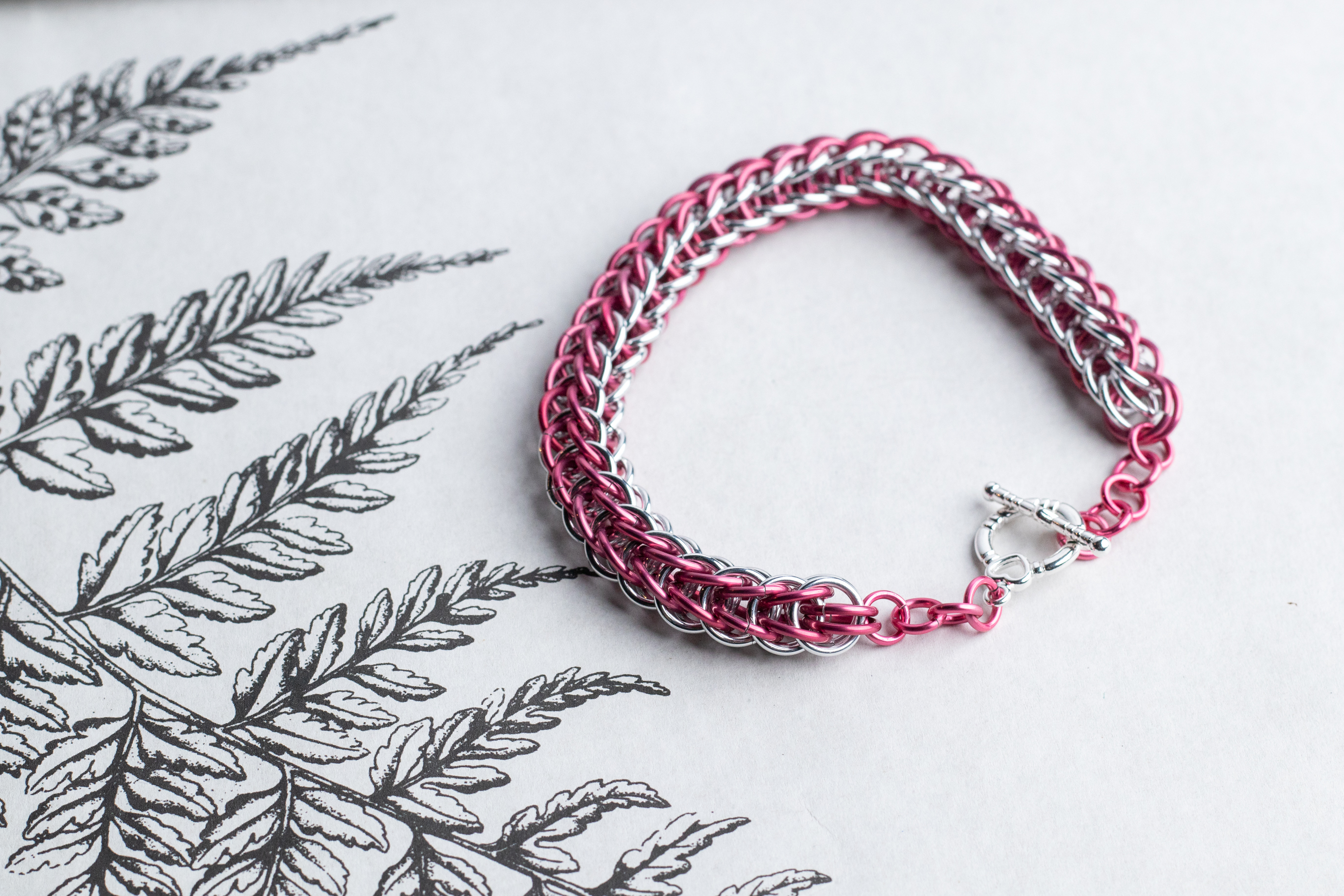 A pink and silver chain bracelet on a white background.