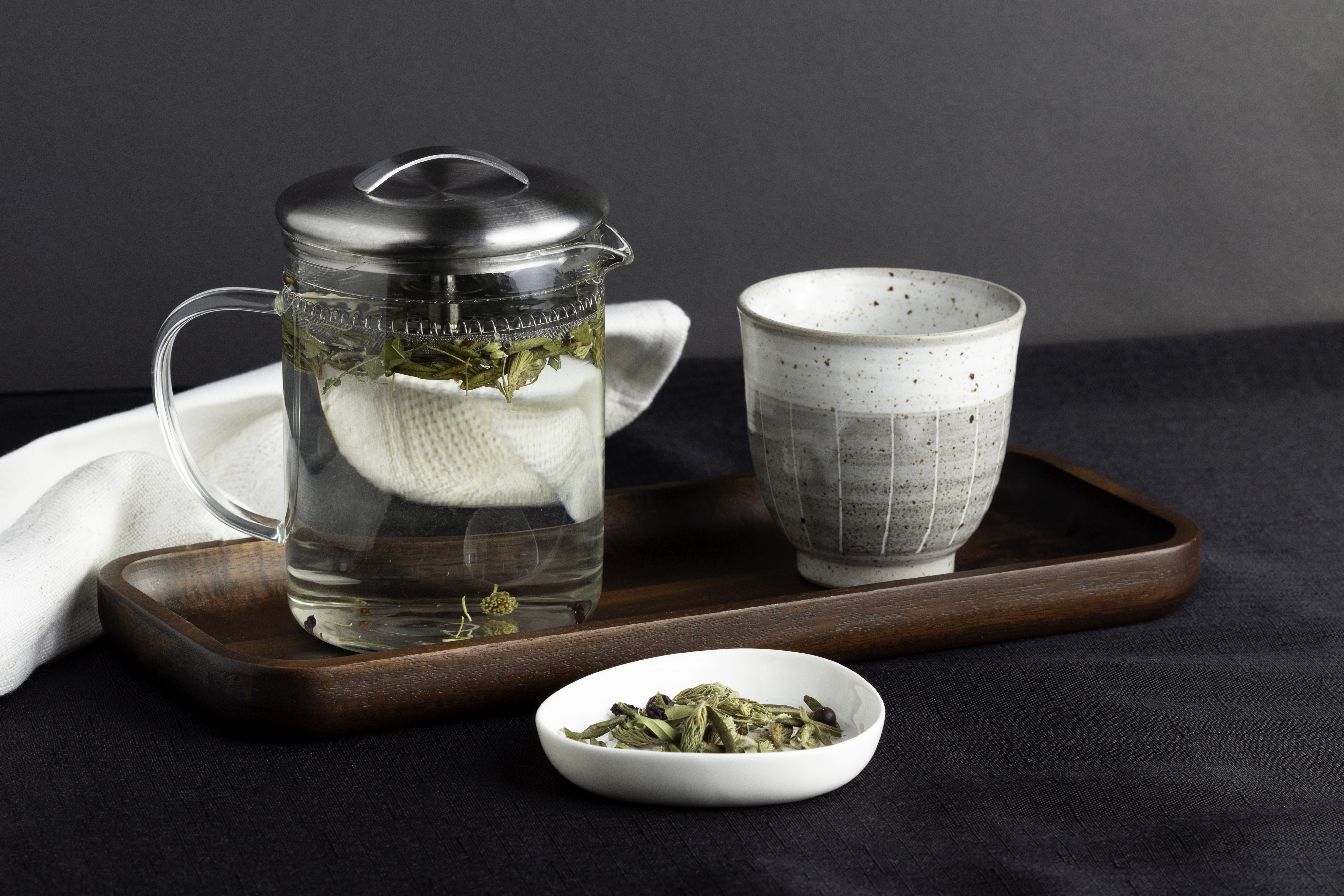 A glass tea carafe and a teacup sitting on a wooden tray on a dark background.