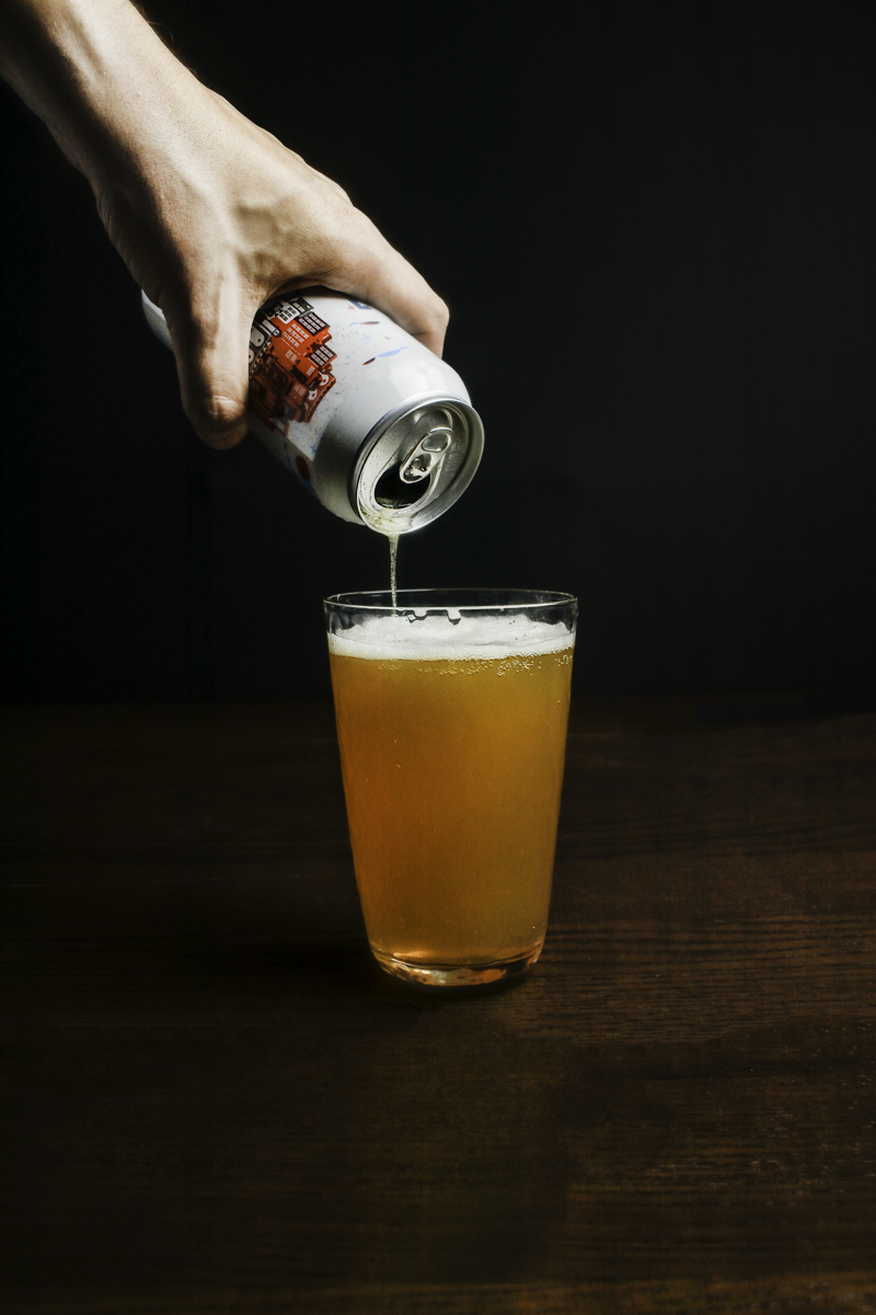 A man's hand pouring a beer from a can into a glass.