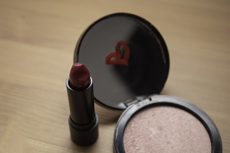 A heart drawn in lipstick on a compact mirror with the lipstick on a table.