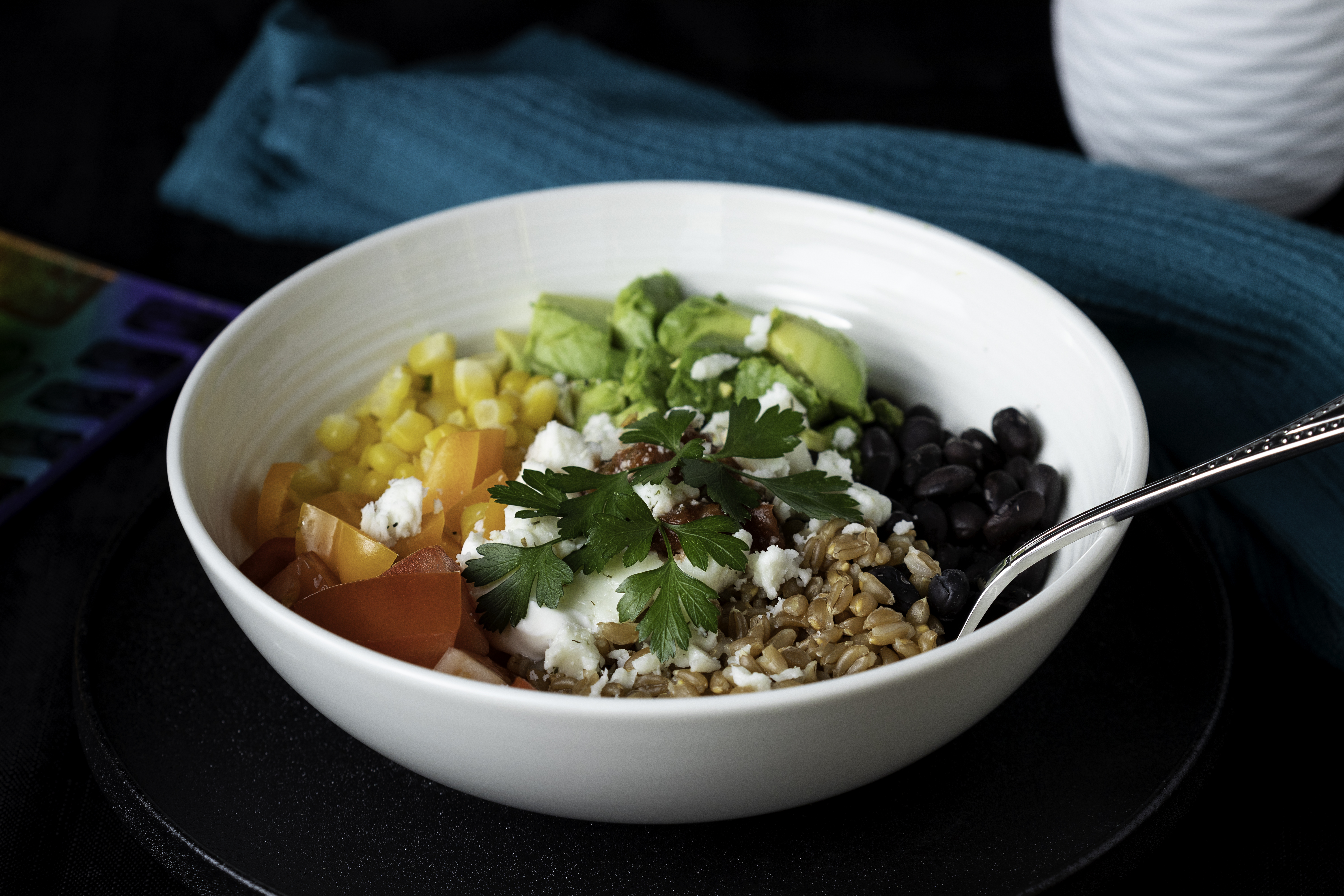 A white bowl filled with fresh ingredients like corn, tomatoes, rice and parsley.