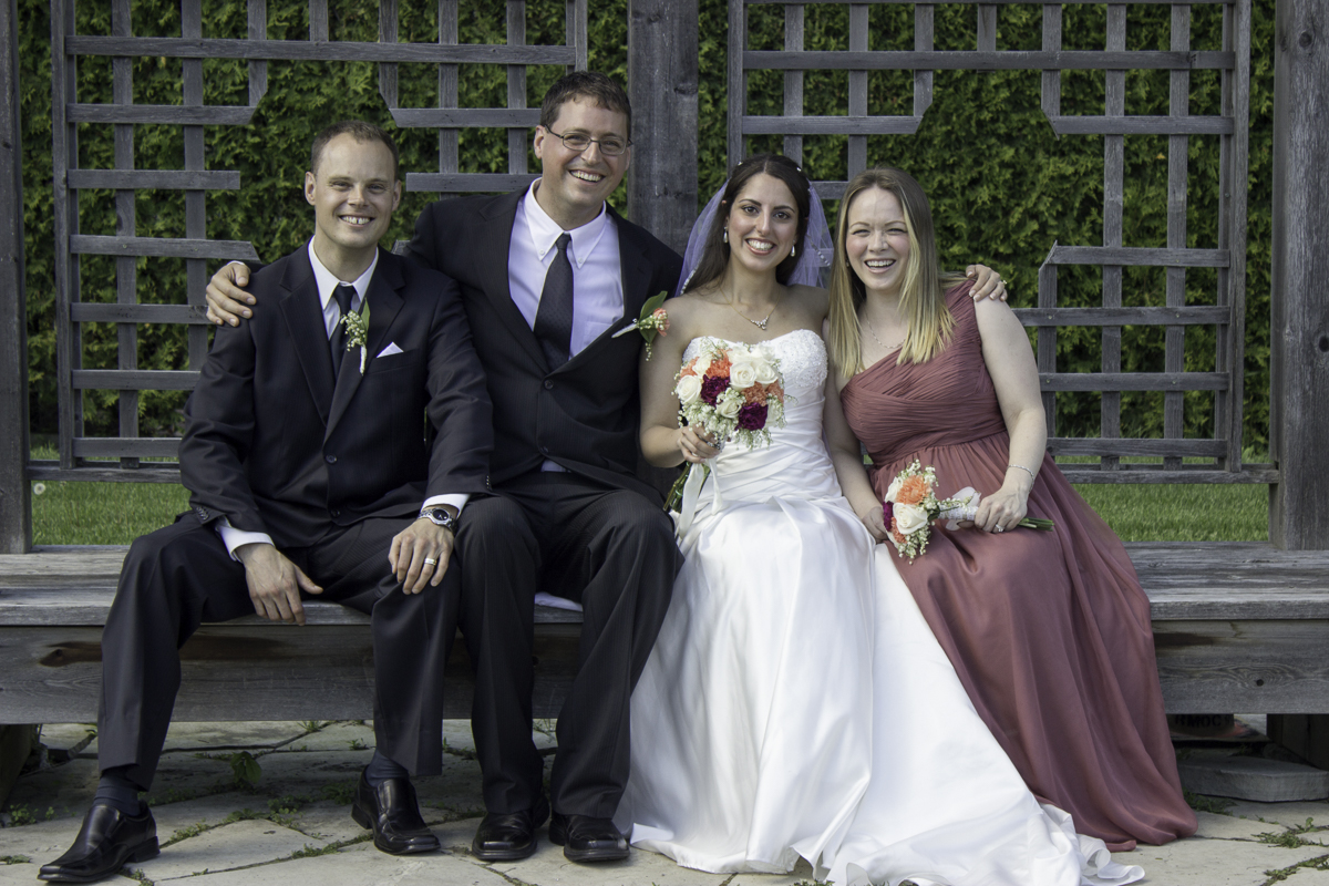 A bride and groom sitting on a bench with their maid of honour and best man.